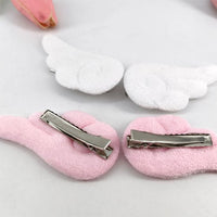 Barrette cheveux en ailes d’ange rose et blanc posées sur planche blanche – deux pairs