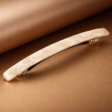 Barrette cheveux blanche marbrée présentée en studio sur fond marron et or.