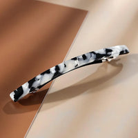 Barrette cheveux blanc et noir présentée en gros plan sur fond crème.