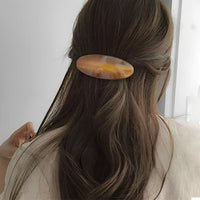 Barrette cheveux ovale caramel fixant une demi-queue élégante sur cheveux longs.