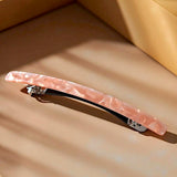 Barrette cheveux rose marbrée présentée en studio sur fond ambre et or.
