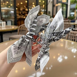 Pince cheveux BandBow blanche tenue en gros plan dans la main d’une femme, vue détaillée du nœud papillon paisley.