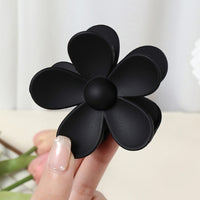 Pince cheveux noire en résine mate tenue par une main féminine.