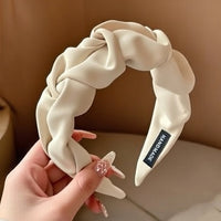 Serre tete UrbanTwist blanc cassé tenu dans la main d’une femme avec volume tressé visible.