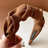 Serre tete UrbanTwist marron café présenté en main avec tissu torsadé structuré.