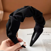 Serre tete UrbanTwist noir présenté dans une main féminine avec finition textile torsadée.